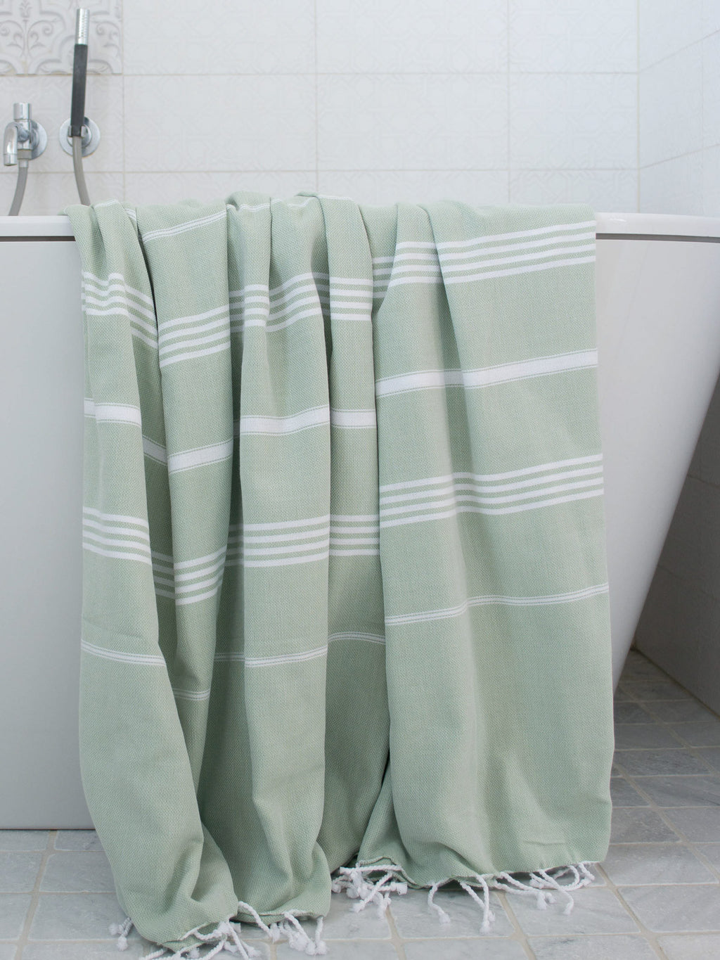 Green towel with white stripes draped over a bathtub in a bathroom setting.