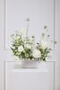 Floral arrangement in a white vase on a white surface with a light gray paneled wall background