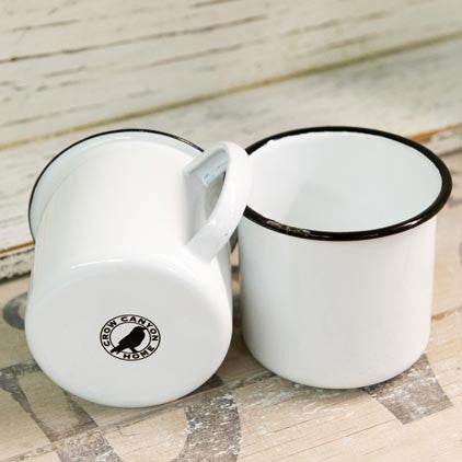 Two white enamel mugs with black rims on a wooden surface