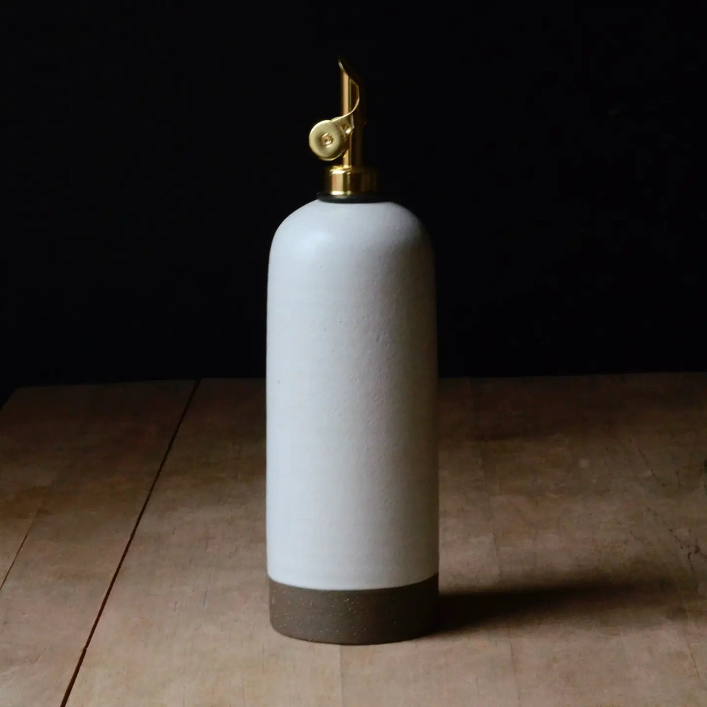 White ceramic oil bottle with gold cap on a wooden surface