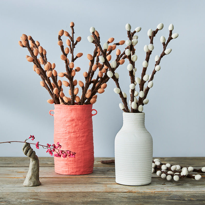 Two vases with decorative felt branches on a wooden surface against a light blue background