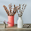 Two vases with decorative felt branches on a wooden surface against a light blue background